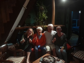 A group of people sitting on a couch in a dimly lit room with a plant and a table with a bowl of snacks. - Hostal La Minga (Chaiten)