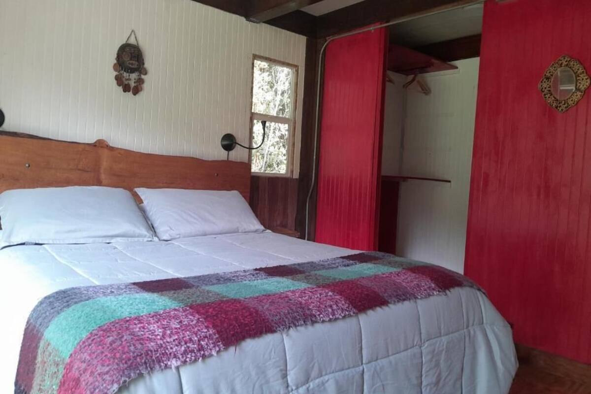 Ein Bett mit Patchworkdecke, einem Holz-Kopfteil, einem Fenster und einem roten Vorhang.