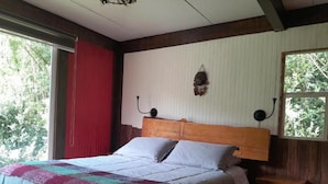 A bedroom with a wooden headboard, a bed with a quilt, a bench, and a wall-mounted light fixture. - Hostal La Minga (Chaiten)