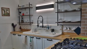 Une cuisine équipée d’une cuisinière à gaz, de meubles blancs, d’un évier et d’étagères remplies d’ustensiles de cuisine.
