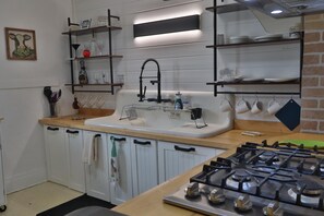 A kitchen with a gas stove, white cabinets, a sink, and shelves with kitchenware. - ALL INCLUSIVE Clean, Safe, and Furnished for those seeking a home away from home (Buffalo)