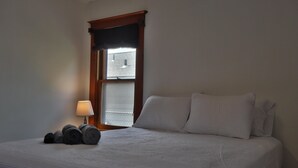 Un lit bien fait, avec du linge de lit blanc, une lampe sur la table de chevet et une fenêtre donnant sur l’extérieur.