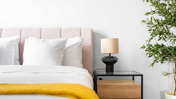A bed with white bedding, a yellow throw, a bedside table with a lamp, and a potted plant. - 1-bedroom Urban Retreat in Prestigious Business Bay (Dubai)