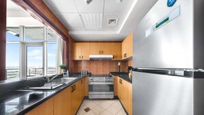 A modern kitchen with wooden cabinets, a stainless steel refrigerator, and a window overlooking a cityscape. - 1-bedroom Urban Retreat in Prestigious Business Bay (Dubai)