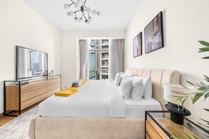 A modern hotel room with a large bed, a TV, a wooden dresser, and a view of the city through the window. - 1-bedroom Urban Retreat in Prestigious Business Bay (Dubai)