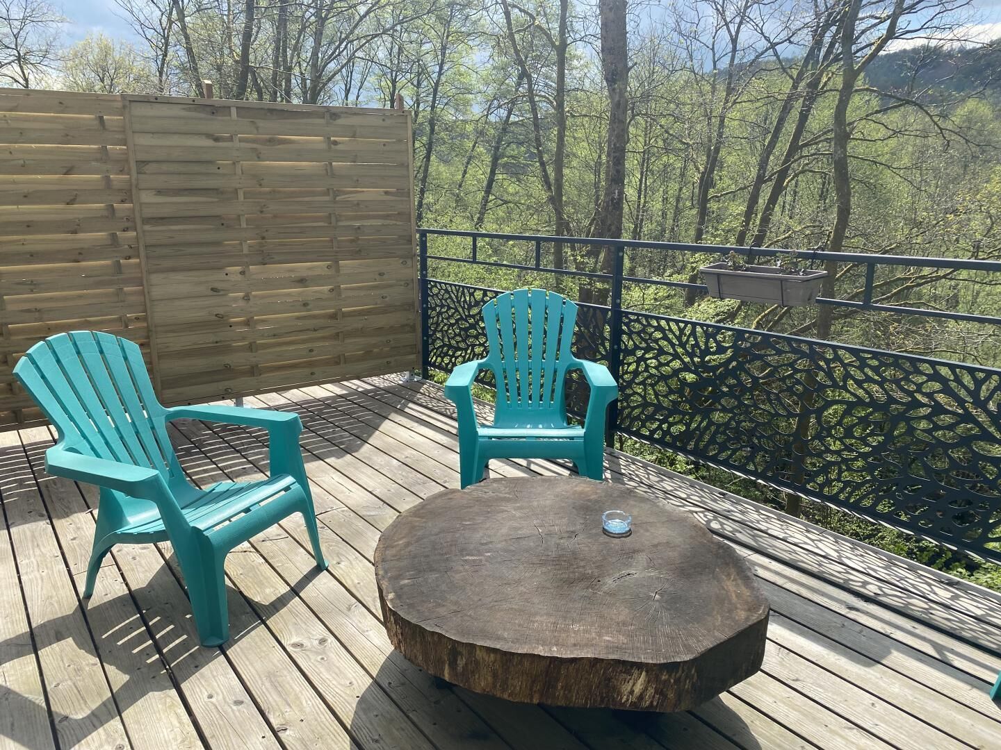 Een houten terras met twee turquoise Adirondack-stoelen en een ronde houten tafel.