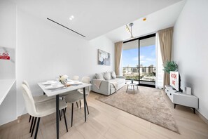 Ein modernes Wohnzimmer mit Essbereich, einer Couch, einem Couchtisch, einem Fernseher und einem großen Fenster mit Blick auf die Stadt.