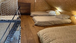 A cozy attic bedroom with a wooden ceiling, a bed with patterned bedding, a small dresser, and a hanging net.
