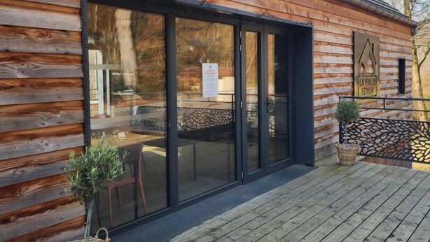 A wooden cabin with a large sliding glass door, a wooden deck, and a sign indicating 'LA HALLE SEMOV.'
