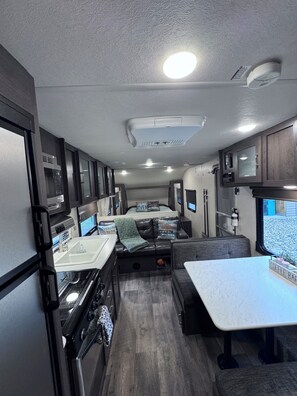 Ein kompaktes Wohnmobil-Interieur mit Küchenzeile, Essbereich und Sitzecke mit Blick aus dem Fenster.