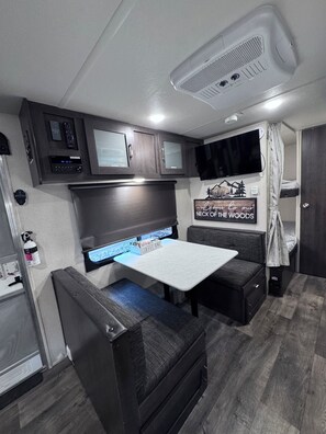 Ein kompaktes Wohnmobil-Interieur mit einer Küchenzeile, einem montierten Fernseher, einer Kaffeebar und einem Stockbett.