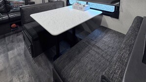 En kompakt autocamper indretning med et tekøkken, et spiseområde med bord og bænk samt et lille vindue med udsigt.