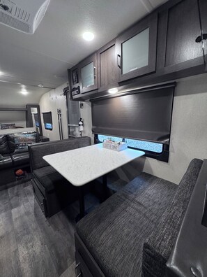 Ein kompaktes Wohnmobil-Interieur mit Küchenzeile, Essbereich mit Tisch und Bank sowie kleinem Fenster mit Aussicht.