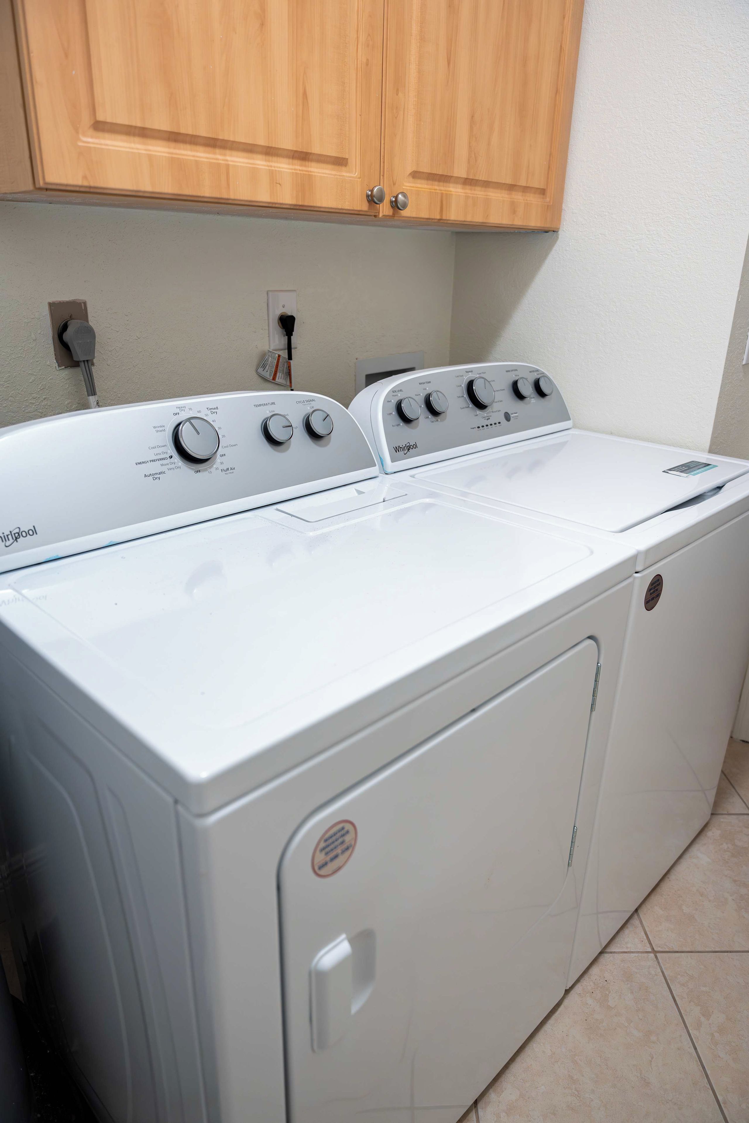 A front view of a Whirlpool washer and dryer unit in a kitchen with wooden cabinets above.