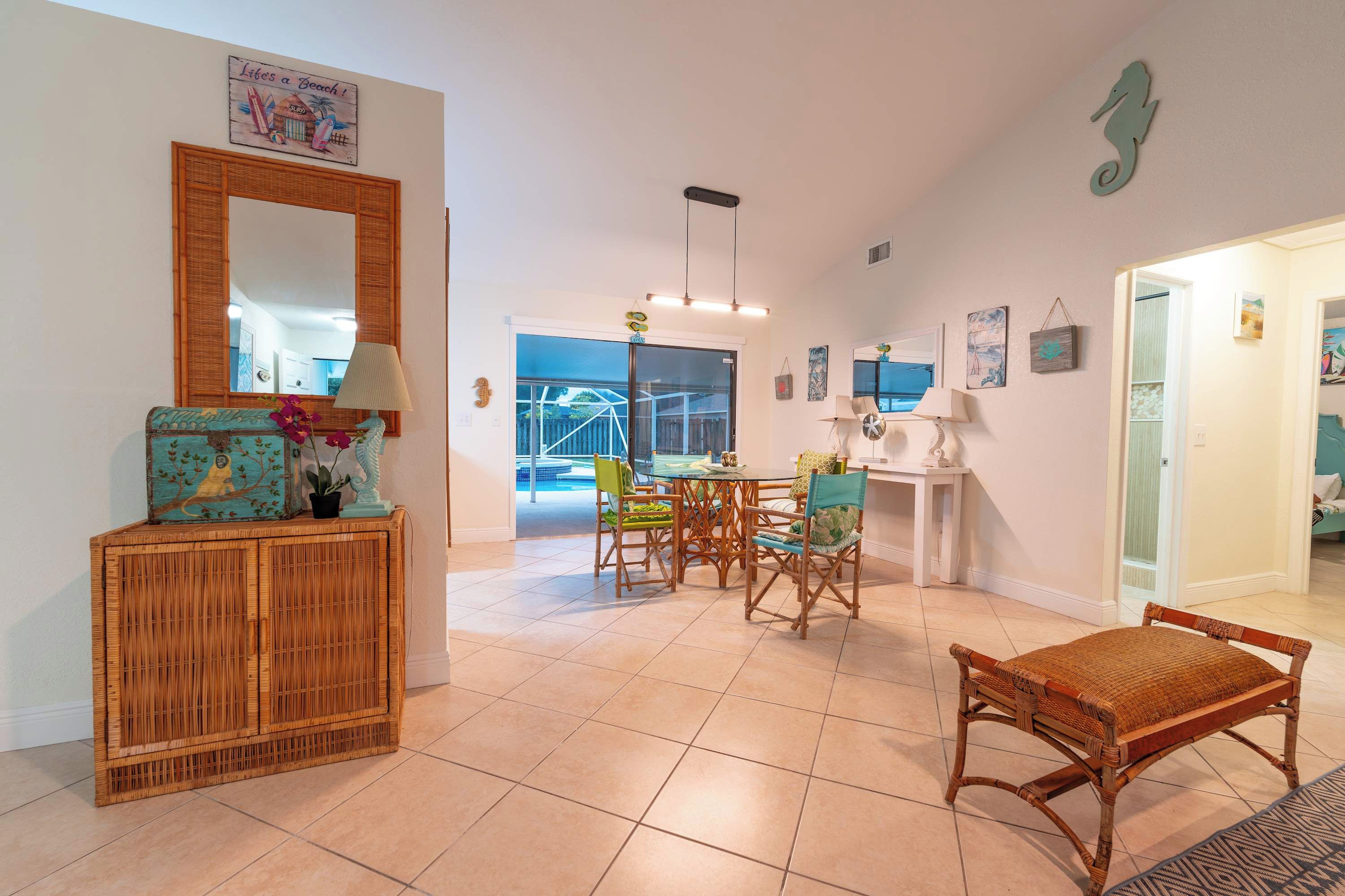 A spacious living area with a dining table, chairs, a wicker bench, and a large mirror.