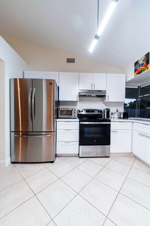 Una cocina moderna con electrodomésticos de acero inoxidable, armarios blancos y piso de baldosas.