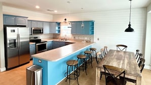 Cozinha moderna com uma ilha central, banquetas de bar e uma mesa de jantar com cadeiras.