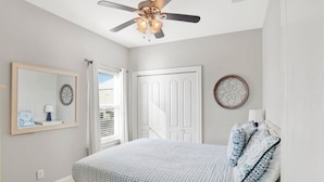 Quarto com cama, ventilador de teto, porta e janela.