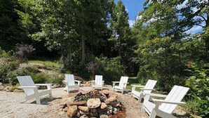 A fire pit surrounded by white Adirondack chairs in a garden setting. - The Outdoor Inn (Lenoir)