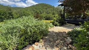 A stone pathway leading through a garden with dense foliage and a view of a forested hill. - The Outdoor Inn (Lenoir)