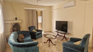 A living room with two blue armchairs, a coffee table, a TV, and an air conditioning unit. - Urban Nest Central Nicosia Spacious 2BR Apartment (Nicosia)