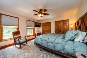 A bedroom with a bed, a rocking chair, a ceiling fan, wooden doors, and a window with blinds. - Private 40-Acre Retreat | Trails, Wildlife & Family Space w/Hot Tub (Nashville)
