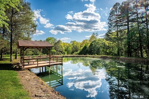 A wooden gazebo over a calm pond, surrounded by lush greenery and tall trees. - Private 40-Acre Retreat | Trails, Wildlife & Family Space w/Hot Tub (Nashville)