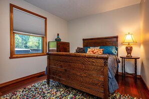 A bedroom with a wooden bed, a window with blinds, a lamp, and a rug.