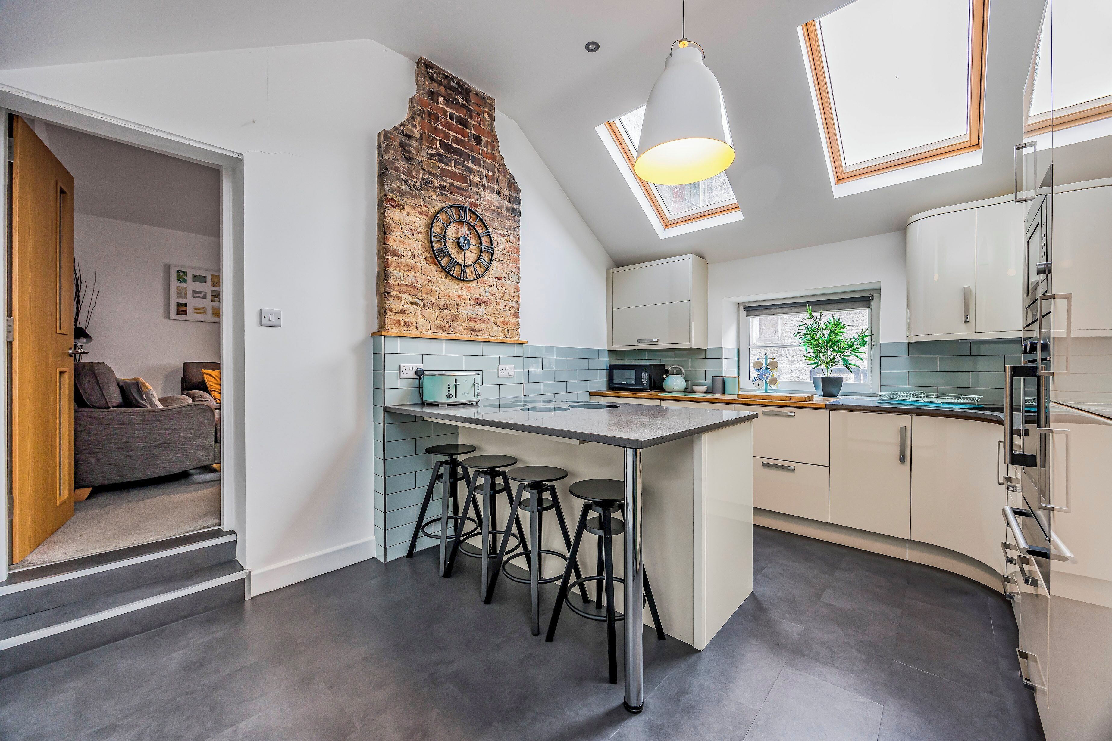 A modern kitchen with a central island, bar stools, a brick accent wall, and skylights.