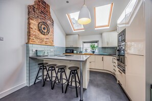 A modern kitchen with a brick accent wall, a large island with stools, and skylights. - Gorgeous, Coastal, Family Flat - Pass the Keys (Bognor Regis)