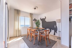 A dining area with a table, chairs, a pendant light, a potted plant, and a bull silhouette on the wall. - 3 Bed with Panoramic Sea views - Pass the Keys (Fuengirola)