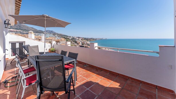 Eine Terrasse mit Tisch und Stühlen, einem großen Sonnenschirm und Blick auf das Meer und die Stadt.