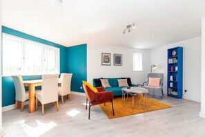 A modern living room with a dining area, a blue accent wall, a sofa set, and a bookshelf. - Modern 2-Bed Apartment Near Kingston - Pass the Keys (Kingston-upon-Thames)