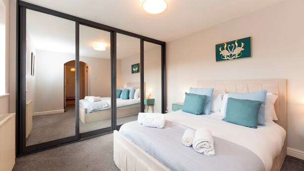 A bedroom with a large mirror, a bed with blue and white bedding, a nightstand, and a wall-mounted artwork. - Modern 2-Bed Apartment Near Kingston - Pass the Keys (Kingston-upon-Thames)