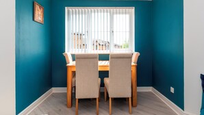 A dining area with a table and chairs, a window with blinds, and a teal wall. - Modern 2-Bed Apartment Near Kingston - Pass the Keys (Kingston-upon-Thames)