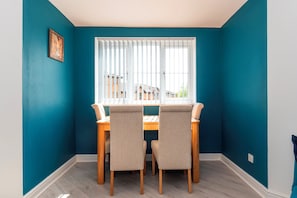 A dining area with a table and chairs, a window with blinds, and a teal wall. - Modern 2-Bed Apartment Near Kingston - Pass the Keys (Kingston-upon-Thames)