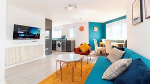 A modern living room with a television, sofa, coffee table, and kitchen in the background. - Modern 2-Bed Apartment Near Kingston - Pass the Keys (Kingston-upon-Thames)