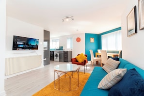 A modern living room with a television, sofa, coffee table, and kitchen in the background. - Modern 2-Bed Apartment Near Kingston - Pass the Keys (Kingston-upon-Thames)