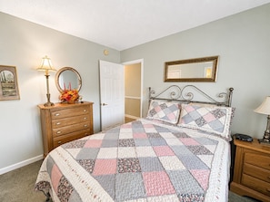 A bedroom with a bed, a dresser, a nightstand, a lamp, a mirror, and a door.