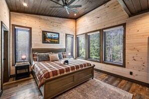 Ein Schlafzimmer mit Bett, Holzwänden, großen Fenstern, einem Deckenventilator und einem Bild an der Wand.