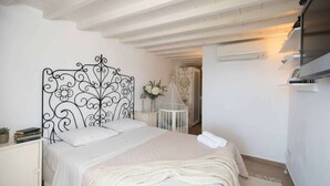 Quarto com cabeceira metálica decorativa, mesa de cabeceira com livros, colcha branca e roupão branco sobre a cama.