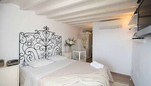 A bedroom with a decorative metal headboard, a bedside table with books, a white bedspread, and a white bathrobe on the bed. - Traditional House in Mykonos Centre (Mykonos)