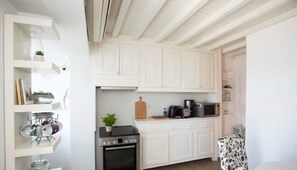 A compact kitchen with white cabinetry, a stove, microwave, and a small dining area. - Traditional House in Mykonos Centre (Mykonos)
