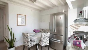 A compact kitchen with a stainless steel refrigerator, a dining table with floral chairs, and a potted plant. - Traditional House in Mykonos Centre (Mykonos)