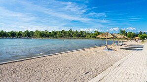 Uma praia com areal pedregoso, água cristalina e uma fileira de guarda-sóis de palha.