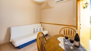 Quarto com sofá, uma mesa de jantar com duas taças de vinho e uma garrafa, luminária no teto e aparelho de ar condicionado.