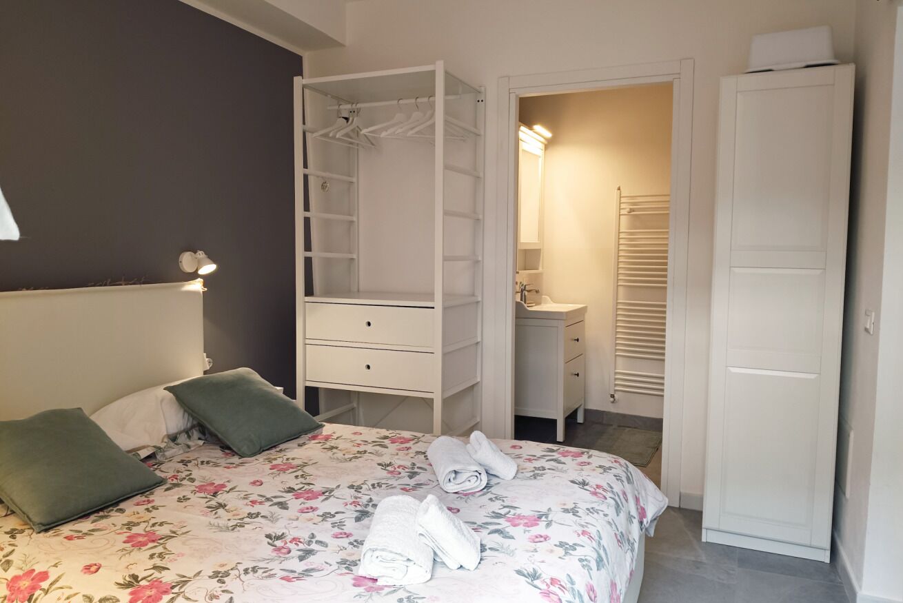 Ein Schlafzimmer mit Bett, begehbarem Kleiderschrank, Bad und einer Tür zu einem weiteren Raum.