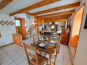 A dining area with wooden tables and chairs, a staircase, and a stone wall in the background. - Breton Stone Cottage by Sandy Beaches (Landeda)