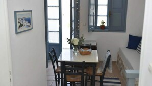A dining area with a table, chairs, a vase with flowers, a basket, and a view of the outside through a door. - Santorini Stay With Hot Tub (Patmos)