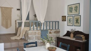 A bedroom with a stone wall, a bed with a canopy, a small table with chairs, and framed botanical prints on the wall. - Santorini Stay With Hot Tub (Patmos)